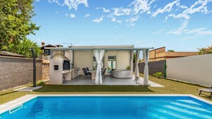 Un jardin avec une piscine, un espace barbecue et un coin salon abrité.
