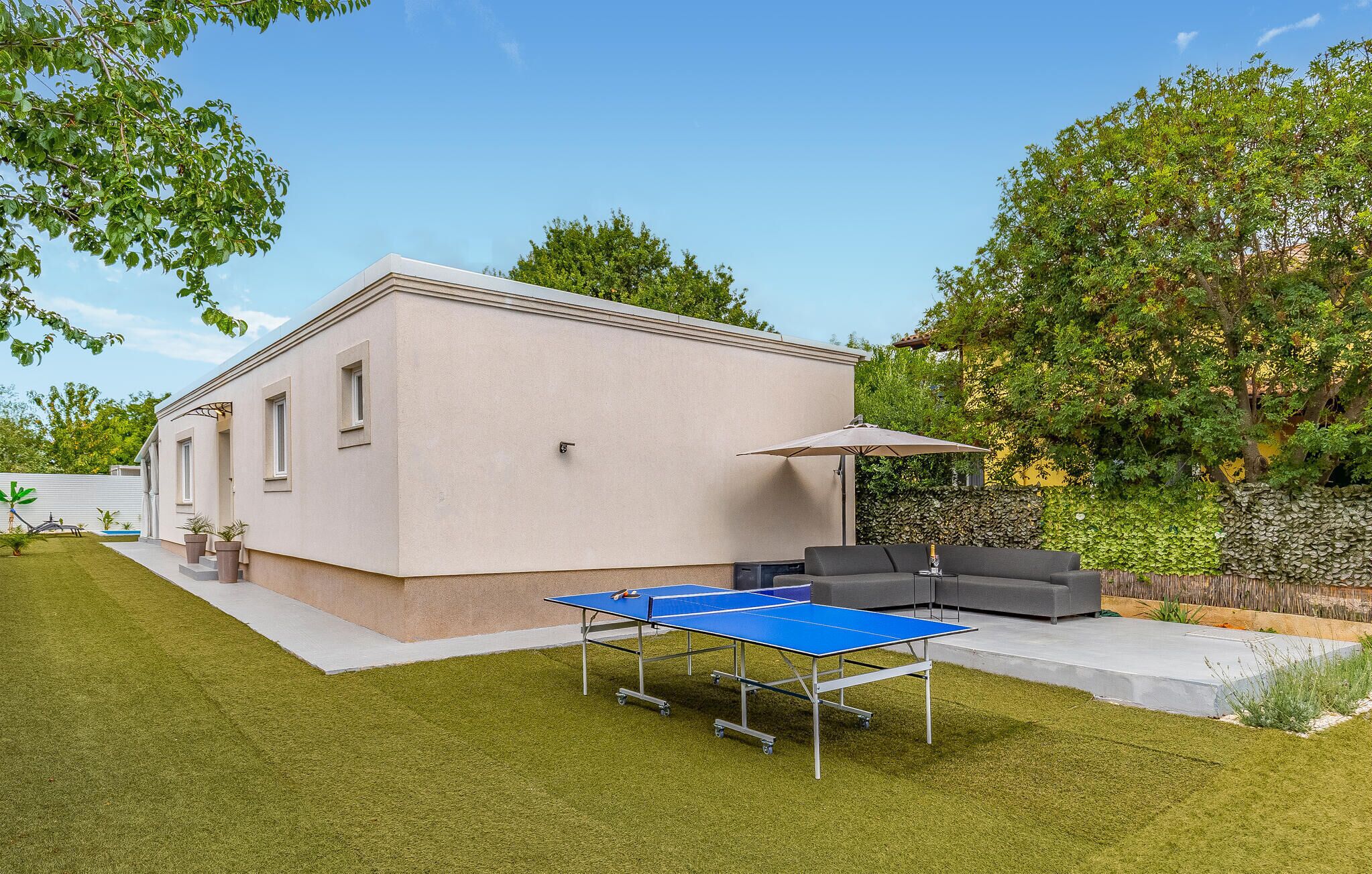 Une maison moderne dotée d’un court de tennis, d’un espace salon extérieur et d’un jardin.