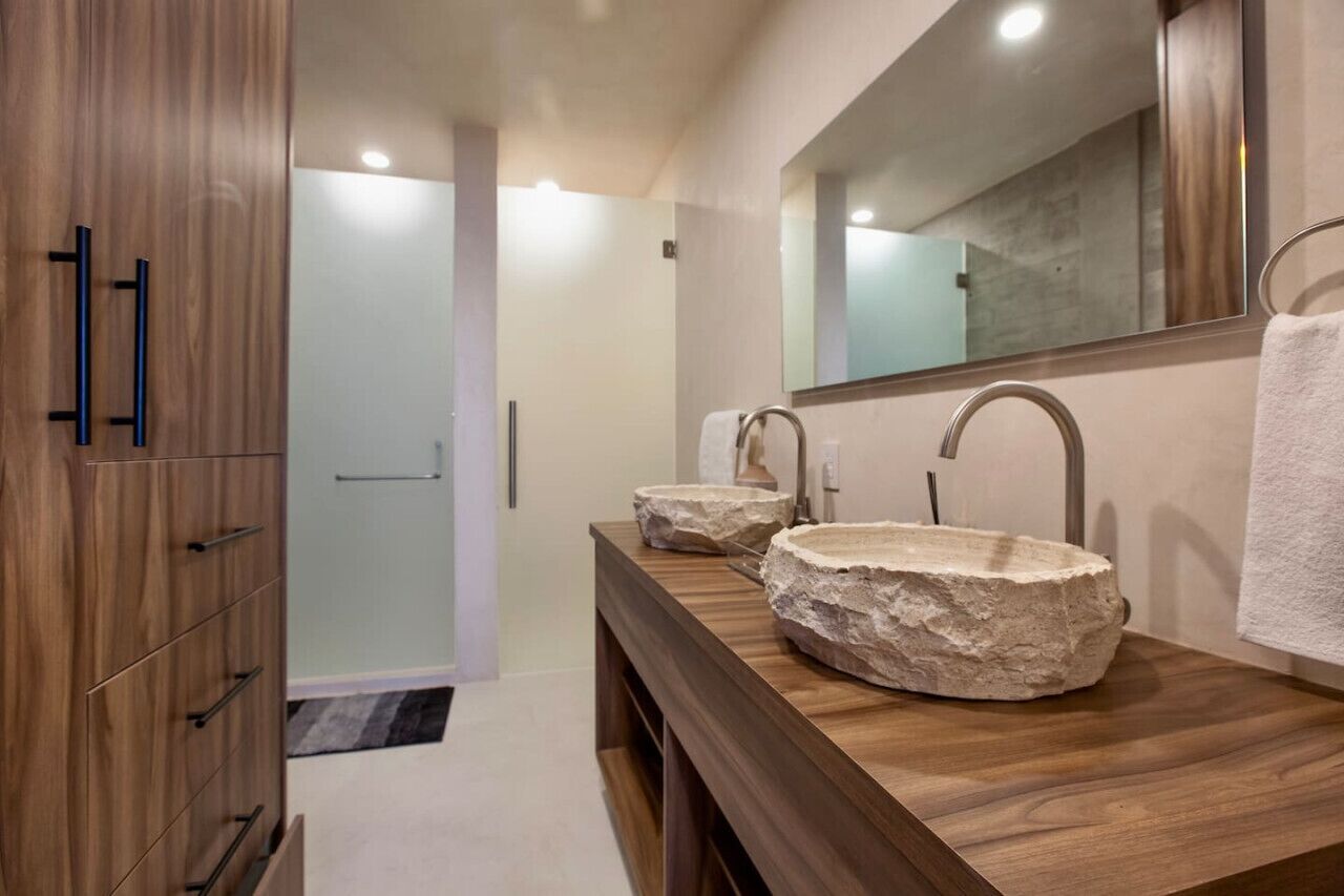 A modern bathroom with a wooden vanity, two stone sinks, and a large mirror.