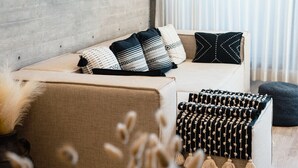 Uma sala de estar moderna com um sofá, almofadas decorativas, luminária pendente e barra de cortina fixada na parede.