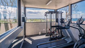 Uma academia moderna com esteiras, um banco de musculação e uma estrutura para agachamento, com amplas janelas e vista para a cidade.