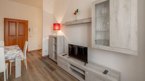Un salon moderne avec un téléviseur, un meuble en bois et un coin repas comprenant une table et des chaises.