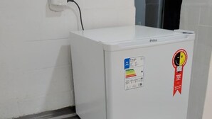 Un refrigerador blanco con un cable de alimentación conectado, una etiqueta que indica eficiencia energética y una etiqueta roja con el logotipo de una abeja.