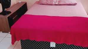 Un dormitorio con cama, mesita de noche, ventilador y piso de baldosas.