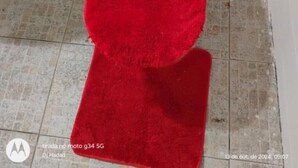 Un baño con una alfombra roja, paredes de azulejos blancos y un inodoro.