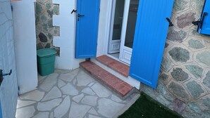 Un pequeño edificio de paredes de piedra con entrada de losas y un césped verde.