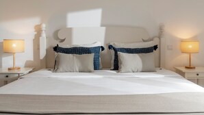 A neatly made bed with white linens, two matching pillows, and a headboard with a unique design. There are two bedside tables with lamps on either side of the bed.