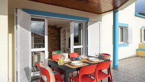An outdoor dining area with a table set for four, surrounded by red chairs, and a wooden ceiling.