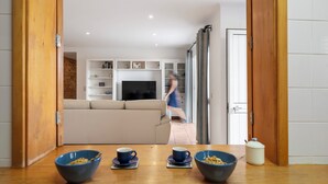 A modern living room with a sofa, a TV, and a dining area with two bowls and cups.
