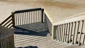Un escalier en bois mène à une plage de sable, d’où l’on a une vue sur l’océan.