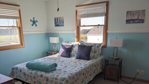 Un dormitorio con una cama, dos mesitas de noche, una ventana y una pared decorada con un cuadro.