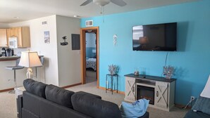 Un salón con sofá, televisión, chimenea y una cocina al fondo.