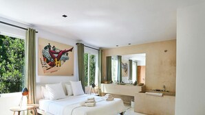 Een moderne slaapkamer met een groot bed, een badkamer met een grote spiegel en uitzicht op groen.