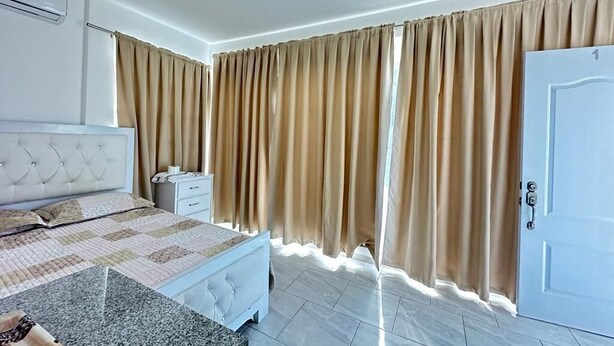 A bedroom with a bed, nightstand, and curtains. - Hotel Peña (Puerto Plata)