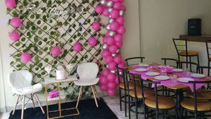 A dining area with a table set for four, chairs, a black rug, and a decorative wall with balloons and greenery. - Hotel Peña (Puerto Plata)