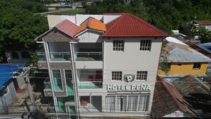A multi-story building with a sign reading "HOTEL PENNA." It features a red roof, multiple balconies, and a mix of glass and metal windows. - Hotel Peña (Puerto Plata)