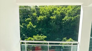 A balcony with a red sofa and ottoman, a glass railing, and a view of dense green foliage. - Hotel Peña (Puerto Plata)