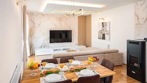 A modern living room with a flat-screen TV, a sofa, a dining table set for four, and a kitchen area with a refrigerator. - Gorgeous home in Lucane (Lucane)
