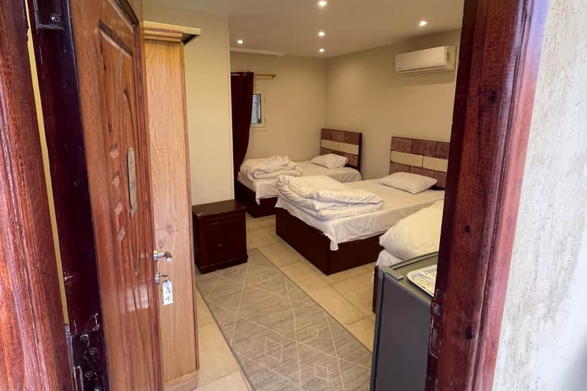 A hotel room with two beds, a bedside table, a small desk, and a wall-mounted air conditioner.