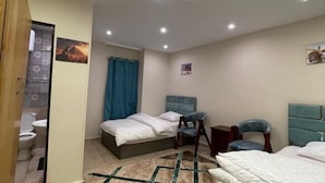 Habitación de hotel con cama, escritorio con una bandeja de tazas, una silla y un baño visible a través de una puerta abierta.