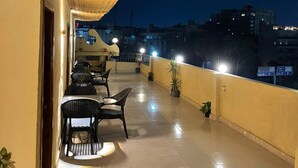 Una terraza en la azotea con techo de paja, mobiliario exterior y vistas nocturnas de la ciudad.
