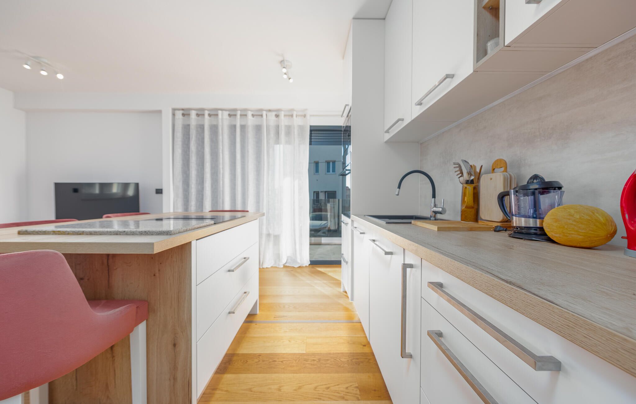 A modern kitchen with a wooden countertop, white cabinets, and a red chair.