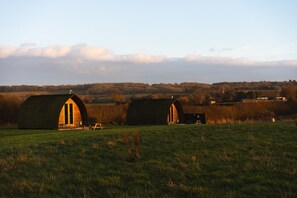 Two barns with arched doorways in a grassy field with a distant view of a hill and a few buildings. - Cosy Rural Cabin with Electric Hot Tub (Grantham)