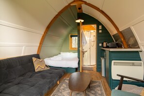Un intérieur chaleureux avec un canapé, un fauteuil, un lit, une douche et un coin cuisine.