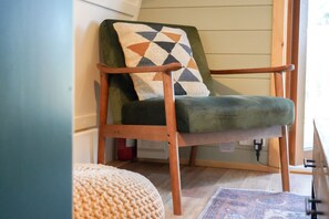A cozy room with a green upholstered armchair, a knitted pouf, and a patterned rug. - Cosy Rural Cabin with Electric Hot Tub (Grantham)