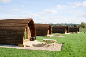 A row of wooden cabins with picnic tables in a grassy field. - Cosy Rural Cabin with Electric Hot Tub (Grantham)