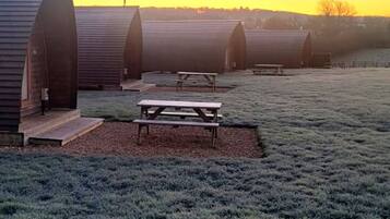 A row of rustic, arched cabins with picnic tables in a frosty field.