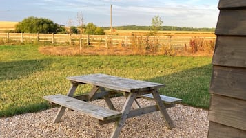 Una mesa de picnic de madera en un área de grava, con un paisaje rural de fondo.