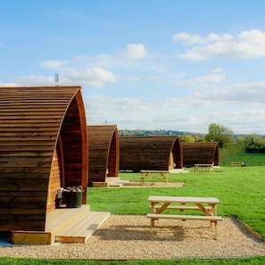 A row of wooden arch-shaped cabins with picnic tables in a grassy field.