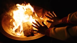A close-up of a hand reaching towards a fire.