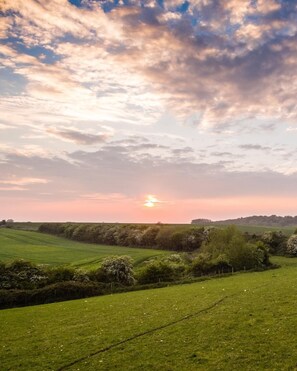 Ländliche Landschaft mit sanften, grünen Hügeln und einem Sonnenuntergang in der Ferne.