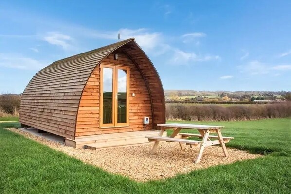 A wooden cabin with a pitched roof, a door, and a picnic table in front.