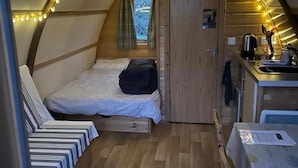 A cozy, compact room with a loft bed, a small kitchenette, and a window with curtains.