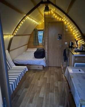 A cozy, compact room with a loft bed, a small kitchenette, and a window with curtains.