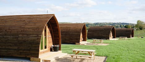 A row of wooden cabins with picnic tables in a grassy field.