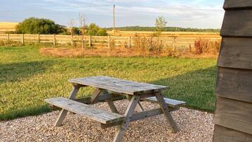 Una mesa de picnic de madera en un área de grava, con un paisaje rural de fondo.