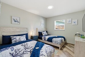 Een slaapkamer met twee bedden, een nachtkastje, een bijzettafeltje en een raam met jaloezieën.