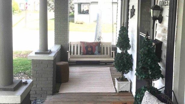 A covered porch with a wooden floor, a bench, and a small Christmas tree.