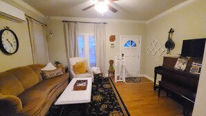 A living room with a brown sofa, a white armchair, a coffee table, a piano, and a ceiling fan.