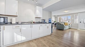 A modern kitchen with white cabinets, a central island, and a dining area with a gray sofa.