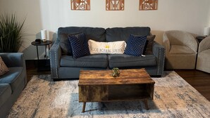 Un salón con un sofá gris oscuro, una mesa de centro de madera y paneles decorativos en la pared.
