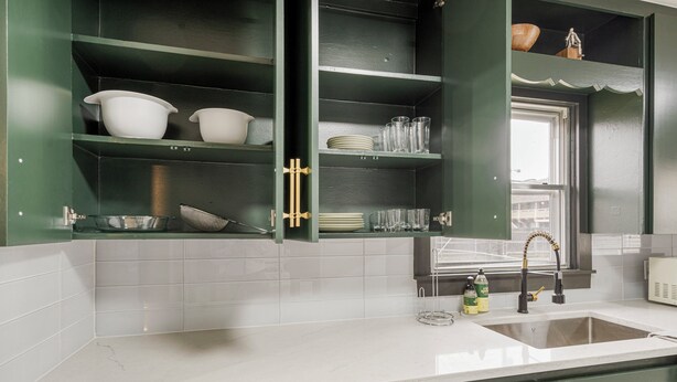 Una cocina con armarios verdes, encimera blanca y ventana sobre el fregadero.