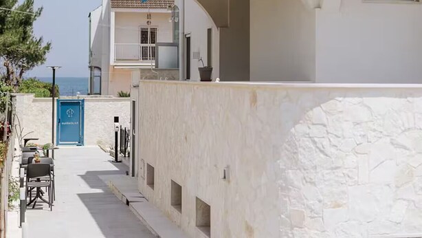 A modern two-story building with a white facade, a blue awning, and a stone wall. - Basic Double Room (Bari)