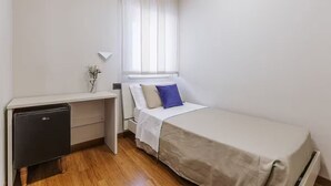 A compact bedroom with a single bed, a small desk, and a compact refrigerator. - Single Room (Bari)