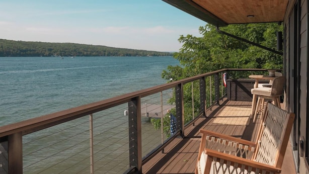 Una terraza de madera con vista a un lago, amueblada con sillas de mimbre y una mesa.