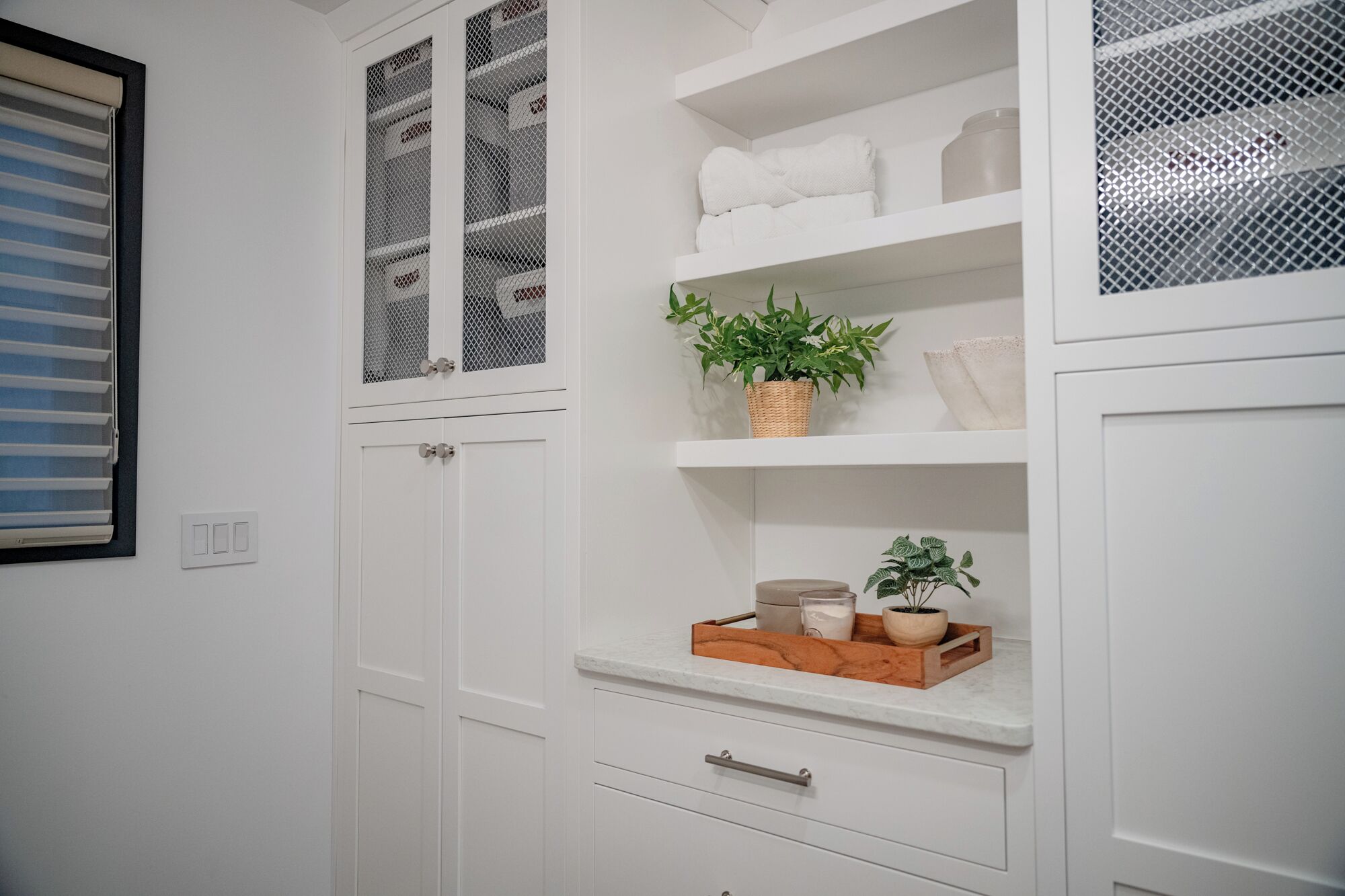 A white bathroom with a window, a towel rack, a shelf with toiletries, and a plant.